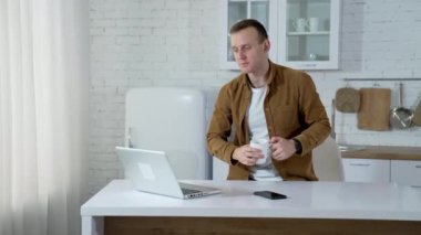 Freelancer dizüstü bilgisayarla konuşuyor. Genç adam mutfakta video görüşmesi sırasında biriyle konuşuyor. Uzak görev.