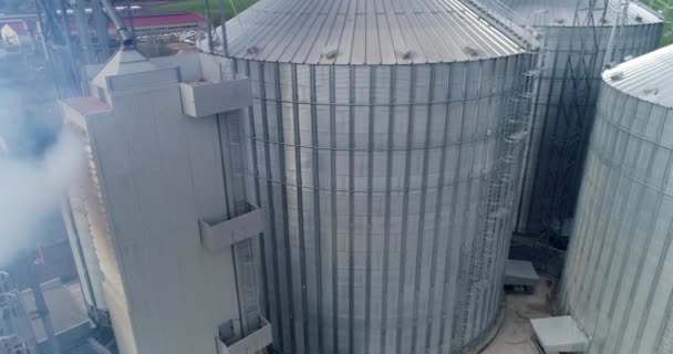 フィールド上のグレーンエレベーター 大きな金属製のおばあちゃんが煙を吸っている 近代的な工場の銀製アルミニウム容器 エアリアルビュー — ストック動画