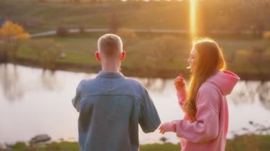 Gün batımında romantik bir çift. Güzel kız ve erkek arkadaşı doğada durup batan güneşe bakıyorlar. Mutlu gençler nehir kenarında konuşuyor..