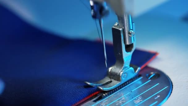 女性の手はミシンを通して材料をプッシュします 縫う機械針は急速に上下に動きます 縫製工場のテーラーは青い生地を縫います クローズアップ — ストック動画