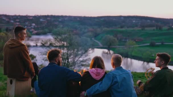 若者は夕方にピクニックをする 美しい自然の背景に火で幸せな時間を過ごす友人のグループ リアビュー — ストック動画