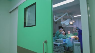 Estetik cerrahi doktorların işi. Ameliyat sırasında ameliyat masasında yatan hasta. Klinikteki operasyonel prosedürü koridordan izle.