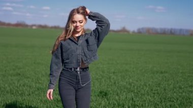 Yeşil sahada genç bir kadının portresi. Kot takım elbiseli güzel, uzun saçlı sarışın kız doğada kameraya bakıp gülümsüyor..