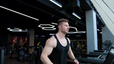 Eğitimli vücutlu yakışıklı bir adam koşu bandında koşuyor. Genç sporcu, modern fitness merkezinde simülatör üzerinde çalışıyor. Sağlıklı yaşam tarzı.