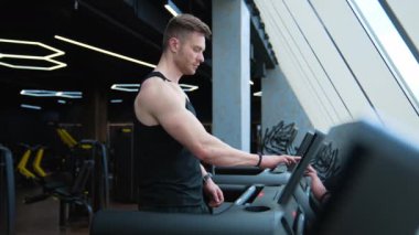 Koşu bandındaki sporcu. Yakışıklı adam, modern fitness kulübünde simülatör eğitimi almaya başlıyor. Sporcu spor salonunda koşu bandında yer değiştiriyor..