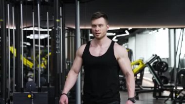 Yakışıklı bir vücut geliştiricinin portresi. Modern fitness merkezinde spor simülatörlerinin arka planında yürüyen kaslı vücutlu genç bir sporcu. Sportif yaşam tarzı.