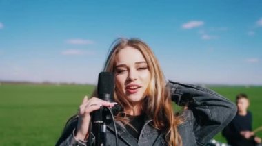 Genç bayan şarkıcı açık havada müzik yapıyor. Doğada mikrofona şarkı söyleyen güzel bir kadın solist..