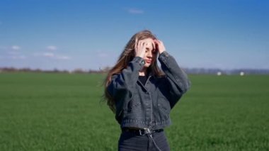 Gün ışığında sahada güzel bir kız. Kot elbiseli genç kadın güneşe kapalı gözlerle ayakta duruyor. Açık havada çekici bir model..