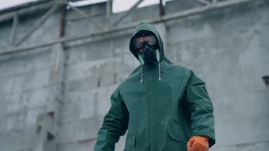 Gaz maskeli adam yıkılmış binanın arka planında. Solunum cihazı ve güvenlik giysisi içinde hayatta kalan radyoaktif bölgede duruyor. Ekolojik bir felaket. Apokaliptik dünya.