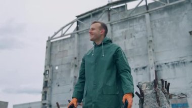 Terk edilmiş bir yerde mutlu bir çevre bilimci. Gaz maskesi tutan ve gülümseyen bir adam yıkılmış binanın arka planında temiz hava soluyor..