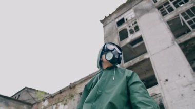 Solunum cihazı ve koruyucu ceketli bir kadın. Penceresiz yıkık binanın arka planında hayatta kalan, şehirdeki kimyasal kirlilik. Aşağıdan görüntüle.