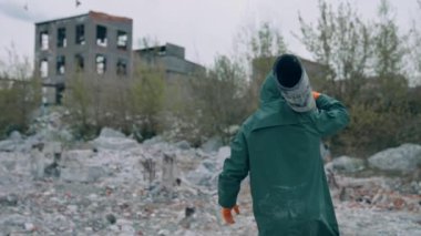 Nükleer kimyasal savaştan sonra hayatta kalan. Kirlenmiş binaların arka planında terk edilmiş borular taşıyan güvenli elbiseli bir adam..