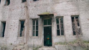 Etkilenmiş bölgede insan. Koruyucu kıyafetli ve gaz maskeli bir ekolojist terk edilmiş binadan çıkıyor ve elinde çiçekler var..