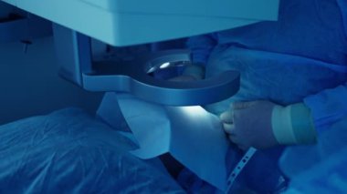 Ameliyathanede göz ameliyatı. Göz cerrahı hastayı lazer görüş düzeltme makinesiyle ameliyat ediyor. Yakın plan. Mavi ışık.