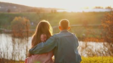 Romantik çift doğada dinleniyor. Genç insanlar birlikte çimenlerde oturup gün batımını seyrediyorlar. Açık havada aşık bir çift..