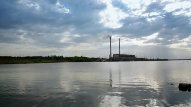 Endüstriyel bölgenin arka planında büyük borularla akşam suyu. Mavi gökyüzünün altındaki fabrika borularından beyaz duman dökülüyor. Çevre kirliliği.