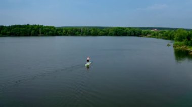 Suda aktif macera. Güzel yaz manzarasının arka planında kürekler olan bir tahtada dururken sporcu su üzerinde antrenman yapıyor. Sıra dışı spor.