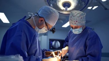 Cerrah ve bayan asistan ameliyathanede. Mavi üniformalı ve maskeli tıp uzmanları klinikteki bir hastaya nörocerrahi uygularlar..