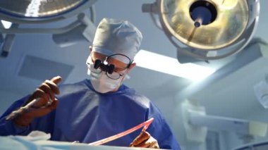 Bir cerrahın yüz portresi. Büyüteç ve maske takan profesyonel bir doktor klinikteki cerrahi lambalara karşı tıbbi aletlerle bir operasyon düzenledi..