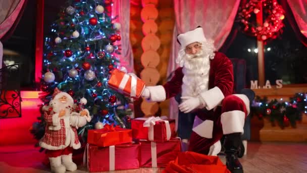 クリスマスプレゼント サンタクロースは大晦日にクリスマスツリーの下にプレゼントを置きます サンタは暖炉の近くに飾られたクリスマスツリーでプレゼントをします — ストック動画