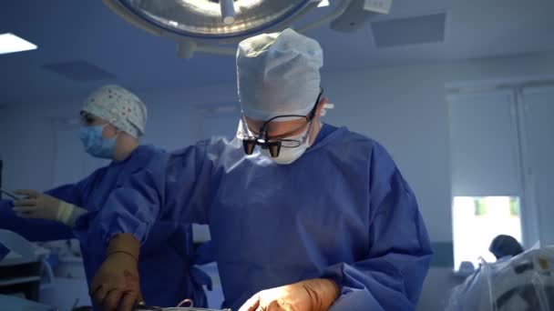 手術劇場での手術 眼鏡と顕微鏡レンズの専門医が神経外科を行っています 外科医に無菌ツールを提供する看護師 — ストック動画