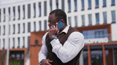 Afrikalı Amerikalı bir adam telefon görüşmesi yapıyor. Kaslı vücutlu neşeli siyahi adam şehir geçmişinde telefonla konuşuyor..