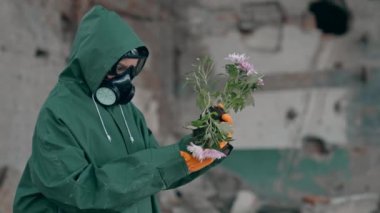 Doğa tehlikede. Güvenlik giysisi ve gaz maskeli bir ekolojist terk edilmiş bir yerde kırık çiçekler tutuyor. Biyokimyasal saldırı. Kirli ortam.