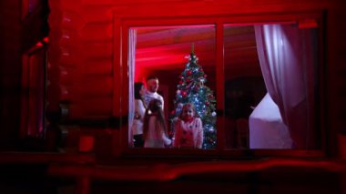 Aile yeni yılı kutluyor. Çift dans ediyor ve çocuklar güzel bir Noel ağacının arka planında pencereye bakıyor. Dışarıdan bak. Kırmızı ışık.