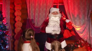 Çocuklu Noel Baba. Beyaz sakallı ve kırmızı takım elbiseli Noel hediyeleriyle dolu bir evde küçük kızlarla konuşan Noel Baba. Aile kutlaması. Kırmızı ışık.