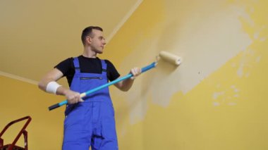 Odada boyama duvarı var. Uzun bir çubukta paten fırçasıyla dairede tadilat yapan profesyonel bir işçi. Aşağıdan görüntüle.