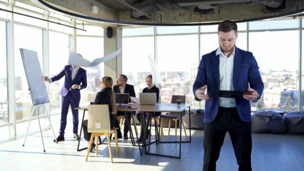 現代のオフィスで働くビジネスマンたち ビジネスマンのグループの背景に青写真を散らすフォルダを持つ若い起業家は話します — ストック動画