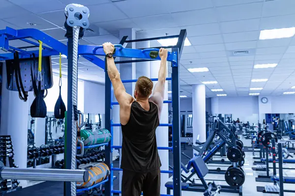 Man Performs Pull-Up Exercise at Gym. A man demonstrates his strength and fitness by effortlessly doing a pull-up at a fully-equipped gym.