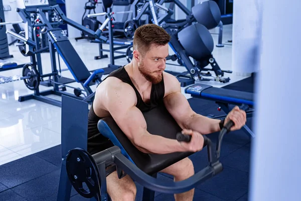 Man Sitting on Gym Bench, Resting After Workout Session. A man sits on a bench in the gym, taking a moment to rest after a workout session.