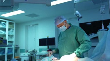 Klinikteki bir hastaya liposuction yapan plastik doktor. Tıbbi üniformalı bir cerrah ameliyathanenin arka planında hastanın karnından yağ pompalıyor..