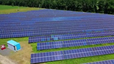 Yeşil doğa arka planında güneş paneli çiftliği. Güneşli bir günde sahada güneş enerjisi santrali. Güneş panelleri güç üretimi için sıra sıra dizildi. Alternatif enerji kaynakları. Hava görünümü.