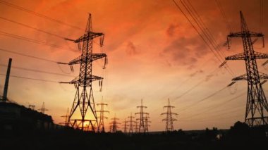 Gün batımında yüksek elektrik kuleleri. Yüksek voltajlı elektrik hattı kablolardan elektrik dağıtır. Akşamları metal direkleri olan dağıtım istasyonu. Yavaş çekim.