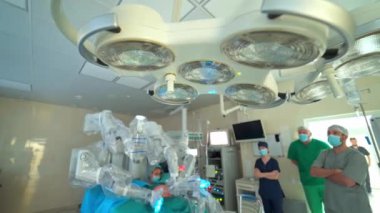Robot ameliyat sırasında cerrahi lambalar kapalı. Klinikteki modern tıbbi ekipmanlar. Bir grup doktor ameliyathanedeki robot cerrahisini gözlemliyor..