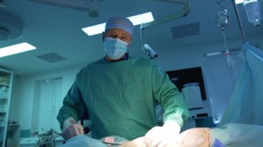 Klinikte liposuction yapan maskeli bir doktor. Profesyonel cerrah ameliyat masasında yatan bir hastaya ameliyat yapar. Ameliyat tedavisi.