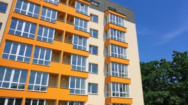 Camlı balkonları olan modern bir bina. Renkli duvarları olan yeni yapılmış apartman bloklarının önü. Şehirde yeni apartman cephesi.