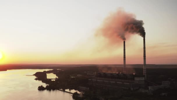 夕暮れの川の近くにある有害な工場 煙突が付いている産業地帯は日没で空気に暗い煙を注ぎます 環境汚染について エアリアルビュー — ストック動画