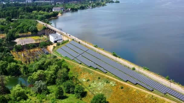 田舎のパワーエネルギーソーラーファーム 明るい夏の日に川の近くにある太陽光発電池 クリーンエネルギーの代替源 エアリアルビュー — ストック動画