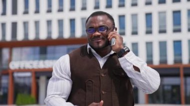 Sportif Afrikalı adam telefonda konuşuyor. Gözlüklü siyahi işadamının portresi şehrin dışındaki telefon görüşmesiyle işyerini yönetiyor..