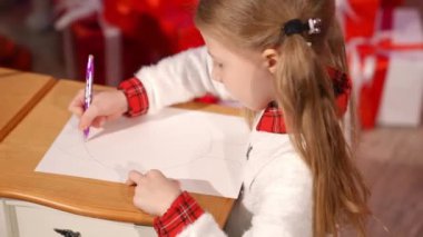 Sevimli çocuk evde bir kalemle resim yapıyor. Küçük kız Noel Baba için odada bir resim çiziyor. Profil görünümü.
