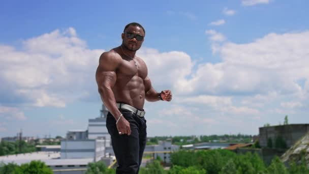 英俊的非洲运动员在户外的肖像 在蓝天的映衬下 站在山丘上 有着强壮的训练过的肌肉的快乐而不穿上衣的运动员 — 图库视频影像