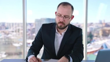 Ofis vitrininde ciddi bir iş adamı. Gözlüklü orta yaşlı işadamı iş yerinde masasında oturuyor. Girişimci iş sorunlarına çözüm arıyor.