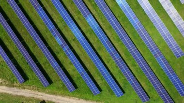 Çağdaş güneş enerjisi çiftliği. Yeşil arazide mavi ve güneşli bataryalar var. Temiz güneşli enerjinin yenilikçi koleksiyoncuları. Üst hava manzarası. Yörünge görünümü.