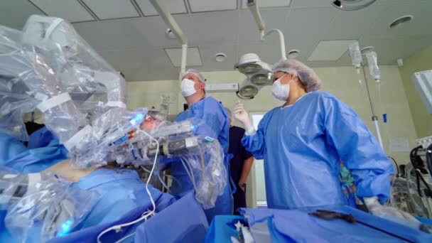 ロボット技術を搭載した病院の外科室 外科医のグループは未来的なオペレーティングルームでマシンアームの近くで働いています 医療ロボットによる最小侵襲手術 — ストック動画