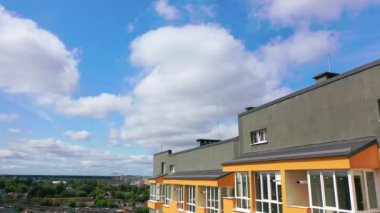 Şehrin modern mimarisi. Şehirde gri çatılı yüksek bir bina. Mavi gökyüzünün altında yeni bir apartman dairesi. Kamera yükseliyor.