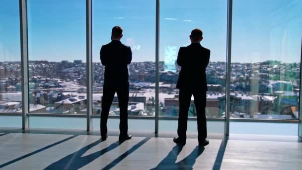 室内で話すスーツを着ているオフィスワーカー 2人のビジネスマンがオフィスに立って窓の外を眺めている リアビュー — ストック動画