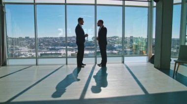 Ofisteki iş ortakları pencere altındaymış. Kostümlü erkek girişimciler büyük pencerenin yanında duruyor ve iş planları hakkında konuşuyorlar..
